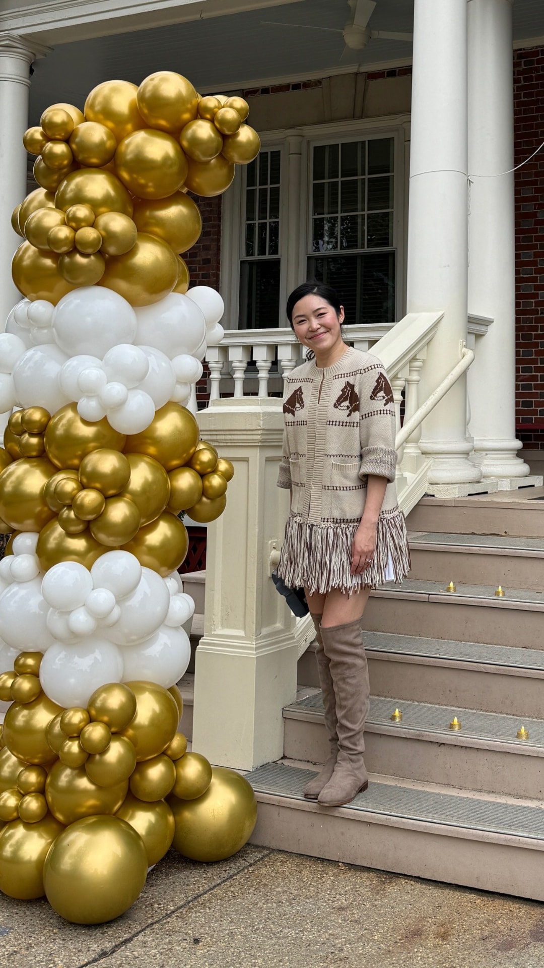 Amanda Lee Liu smiling on porch steps beside a gold and white balloon column.